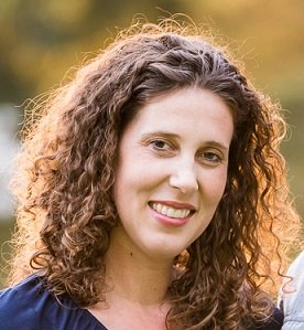 A woman with curly hair smiles warmly at the camera.
