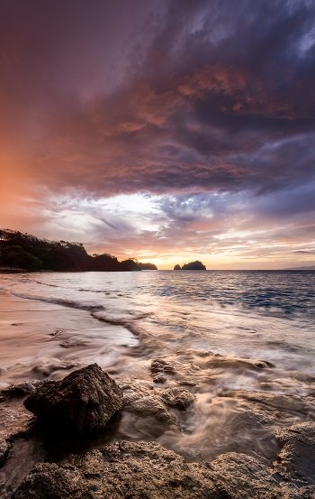A scenic beach featuring smooth rocks and gentle waves lapping at the shore.