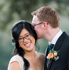 A man leans in close, whispering into a woman's ear with a warm expression.